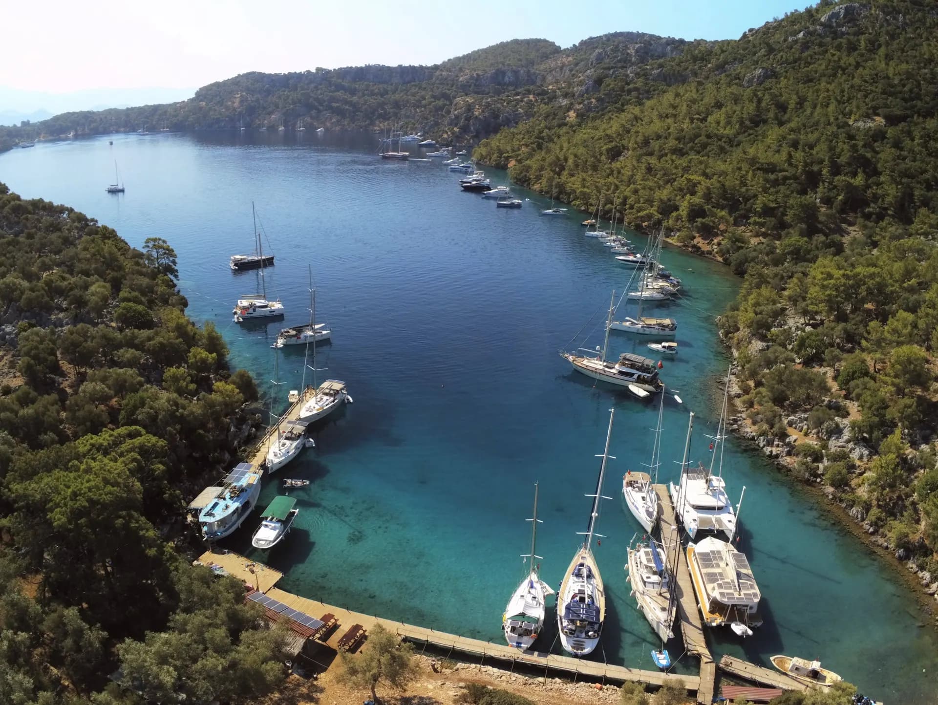 A hidden pine-lined cove with boats moored at a waterfront dining spot